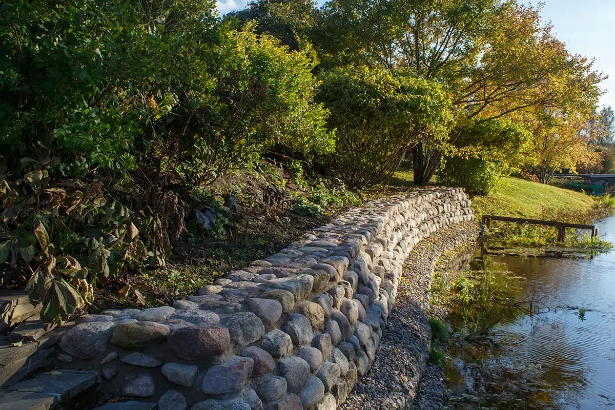 Rounded stone retaining wall following the edge of a waterway, with trees behind